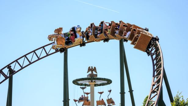Eine Achterbahn mit Fahrgästen fährt durch einen Freizeitpark.