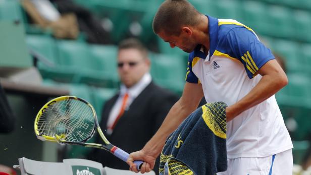 Ein Tennisspieler wischt sich mit einem Handtuch den Schweiß ab, während sein Schläger neben ihm liegt.