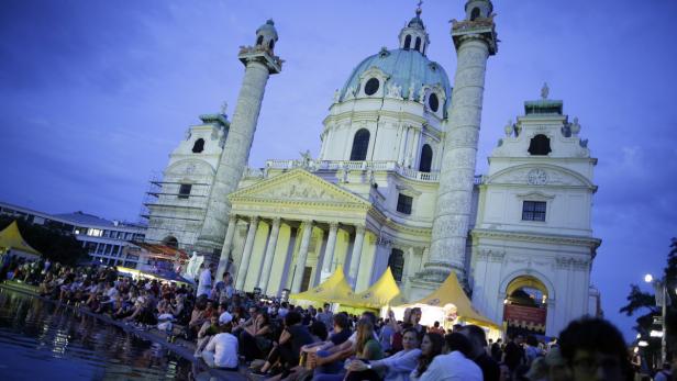 Die Karlskirche in Wien mit einer Menschenmenge davor am Abend.