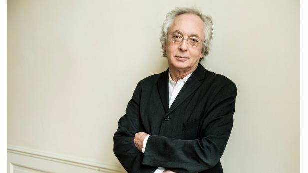 Porträt eines Mannes mit Brille und dunklem Anzug, die Arme verschränkt.