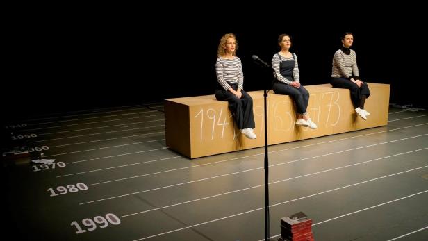 Drei Frauen sitzen auf einer Bank mit den Jahreszahlen 1941, 1963 und 1973 auf einer Bühne.