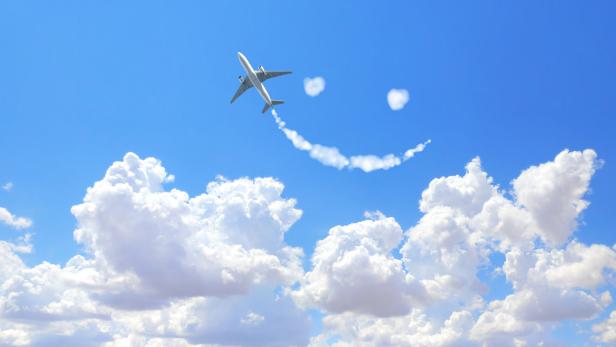 Ein Flugzeug zieht eine Rauchspur in Form eines Smileys in den blauen Himmel.