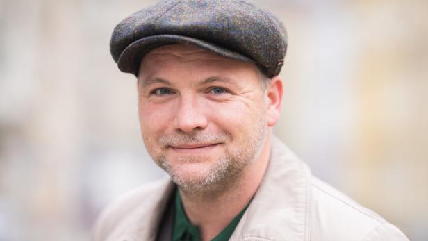 Ein Mann mit Schiebermütze lächelt in die Kamera.