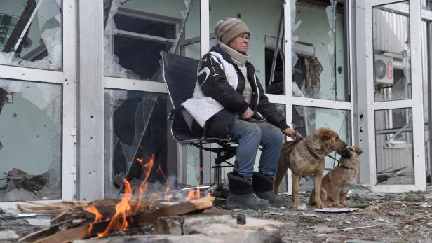 A woman sits outside a damaged building in Volnovakha