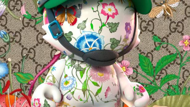 Eine stilisierte Katze mit Blumenmuster, einer grünen Kappe mit der Zahl 100 und einem Gucci-Hintergrund.