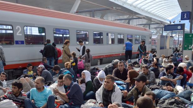 Viele Menschen sitzen oder liegen am Bahnsteig vor einem Zug.