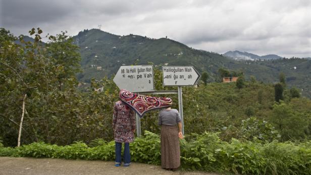 Zwei Frauen stehen an einem Wegweiser in einer grünen Landschaft.