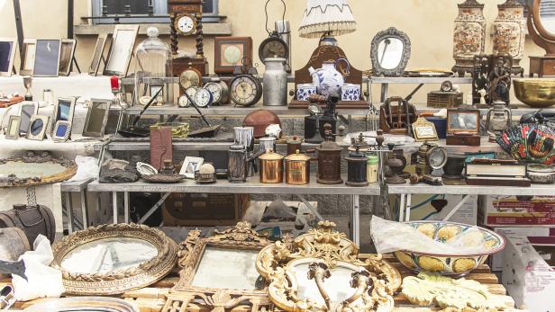 Ein Marktstand mit einer Vielzahl von antiken Gegenständen, darunter Spiegel, Uhren und Lampen.