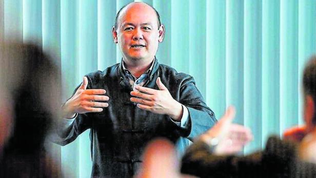 Ein Mann asiatischer Herkunft gestikuliert vor einer Gruppe von Menschen.