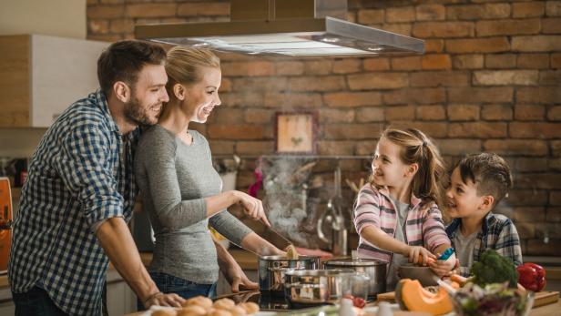 Eine Familie kocht gemeinsam in einer Küche mit Backsteinmauer.