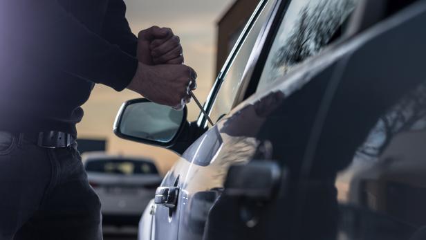 Auto thief in black balaclava trying to break into car