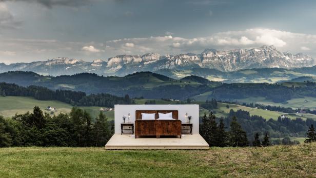 Ein Bett steht auf einer Plattform mit Blick auf eine grüne Landschaft und Berge.
