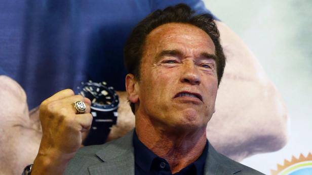 Arnold Schwarzenegger ballt die Faust vor einer Werbewand.