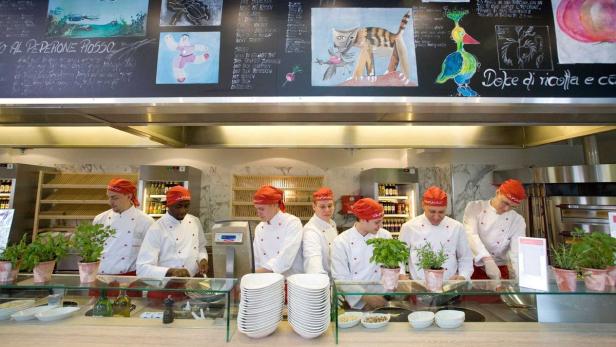 Mehrere Köche in roten Mützen arbeiten in der offenen Küche eines Vapiano-Restaurants.