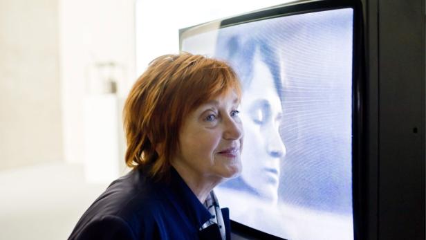 Eine Frau mit roten Haaren schaut auf einen alten Fernsehbildschirm.