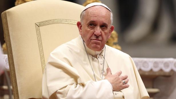 Papst Franziskus sitzt auf einem Stuhl und hält eine Hand auf seine Brust.