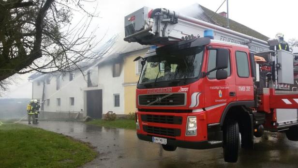 Ein Feuerwehrauto steht vor einem brennenden Gebäude, während Feuerwehrleute den Brand bekämpfen.