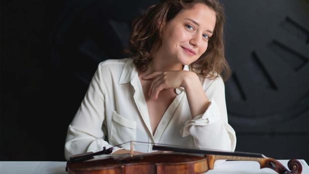 Eine junge Frau sitzt mit einer Geige an einem Tisch.