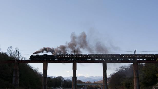 Eine Dampflokomotive fährt über eine hohe Brücke.