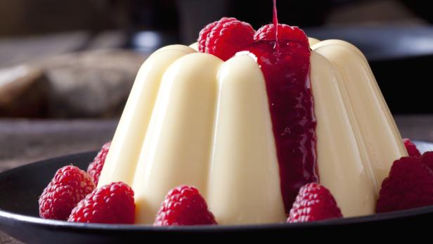 Ein Pudding wird mit Himbeersoße übergossen und mit frischen Himbeeren garniert.