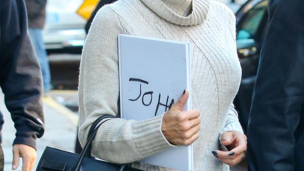 Pamela Anderson mit einer schwarzen Baskenmütze und einer Tasche, die ein Buch mit der Aufschrift „John“ hält.