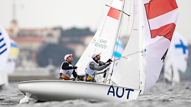 Zwei Segler aus Österreich steuern ein Segelboot mit rot-weißen Segeln.