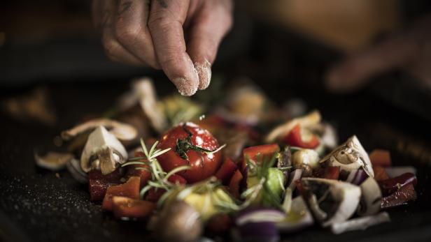 Eine Hand würzt eine Mischung aus Gemüse mit Salz.