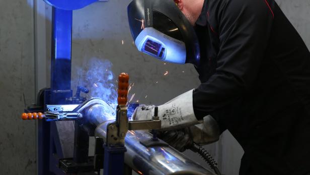 Ein Schweißer arbeitet mit Schutzkleidung an einem Metallrohr.