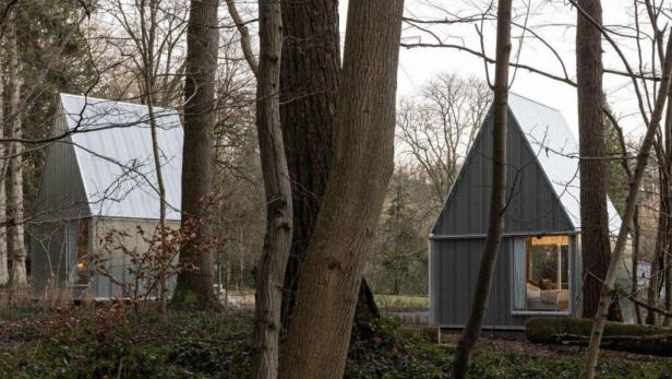 Zwei moderne Hütten mit Metalldach stehen in einem Wald.