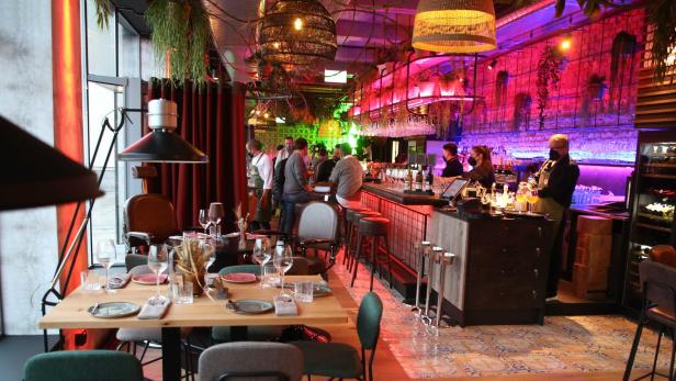 Innenansicht eines Restaurants mit Tischen, Stühlen und einer Bar.