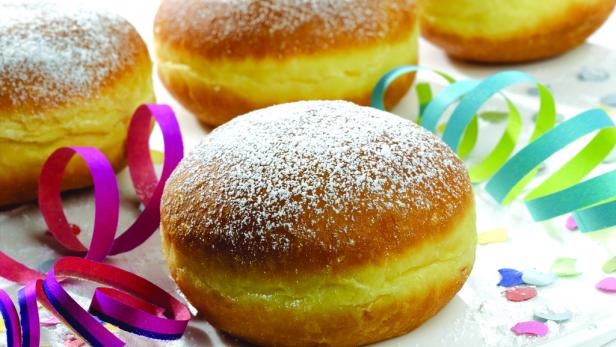 Mehrere Berliner Pfannkuchen mit Puderzucker und bunten Luftschlangen auf einem Teller.