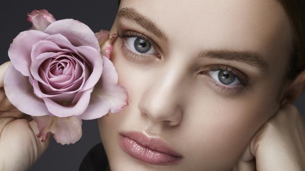 Das Porträt einer Frau mit einer rosa Rose vor ihrem Gesicht.