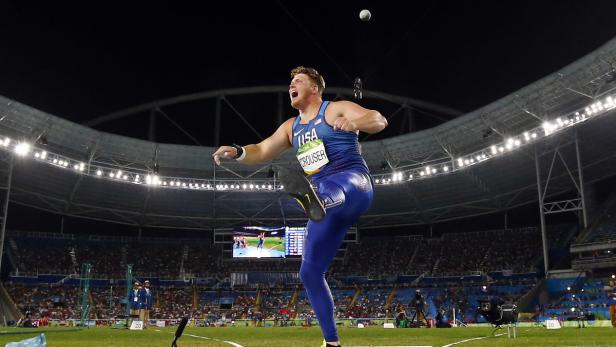 Ein Kugelstoßer im blauen Trikot der USA beim Abwurf in einem Stadion.