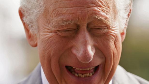 König Charles lacht mit geschlossenen Augen.