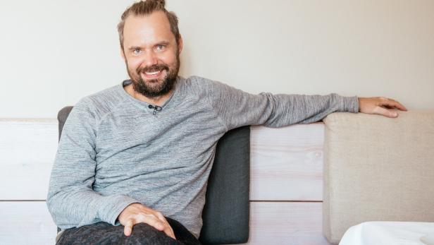 Ein lächelnder Mann mit Bart sitzt auf einer Bank.