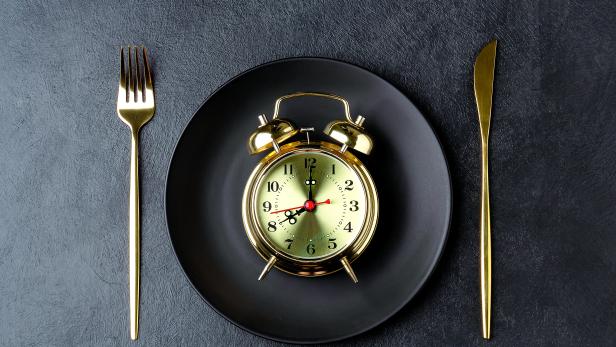Golden alarm clock on a black plate with a golden knife and fork