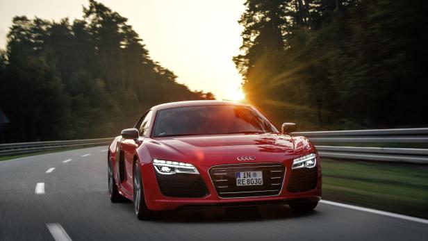 Ein roter Audi R8 fährt auf einer Straße durch einen Wald bei Sonnenuntergang.