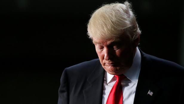 Donald Trump mit gesenktem Kopf vor dunklem Hintergrund.
