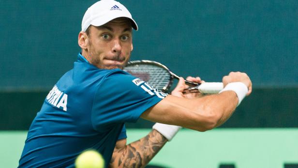 Ein Tennisspieler mit Tätowierungen schlägt einen Ball.