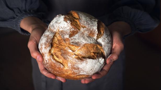 Ein Laib Sauerteigbrot wird von Händen gehalten.