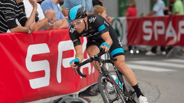 Ein Radrennfahrer in schwarzer Sportbekleidung und blauem Helm fährt ein Rennen.