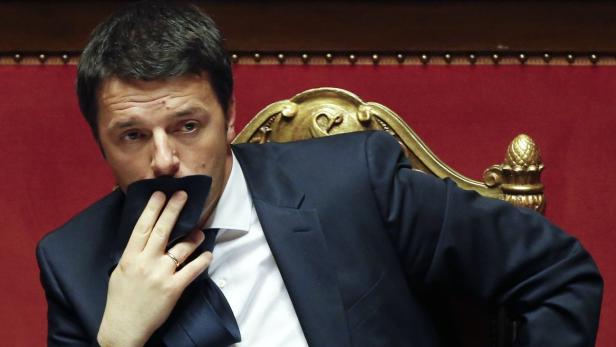 Ein Mann im Anzug sitzt auf einem goldenen Stuhl und hält ein Tuch vor sein Gesicht.