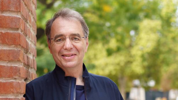 Ein Mann mittleren Alters lehnt an einer Backsteinmauer.