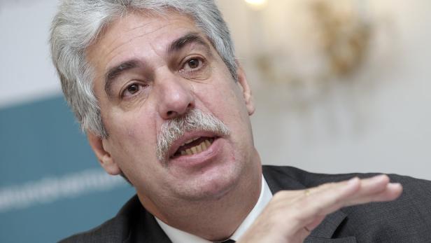 Ein Mann mit grauem Haar und Schnurrbart gestikuliert.