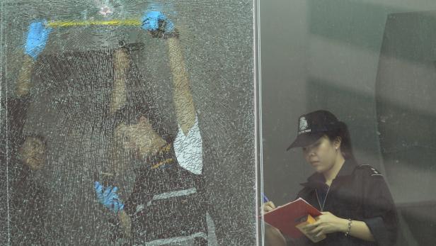 Polizisten untersuchen ein zerbrochenes Fenster und machen Notizen.