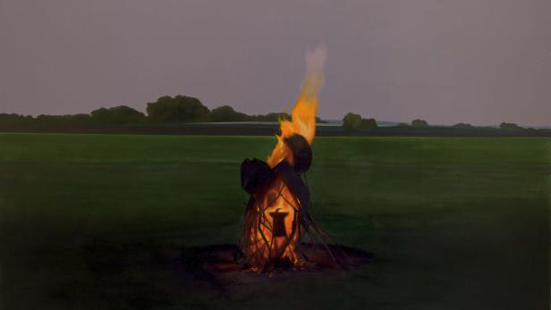 Ein Lagerfeuer brennt auf einem grünen Feld unter einem grauen Himmel.
