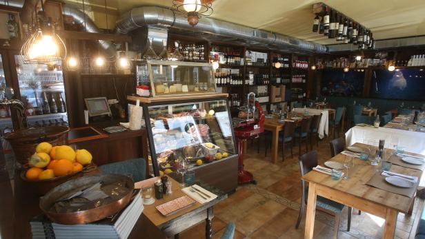 Innenansicht eines Restaurants mit Tischen, Stühlen und einer Theke mit Speisen.