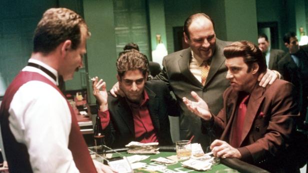 Mehrere Männer sitzen an einem Tisch mit Geld und Getränken, möglicherweise bei einem Pokerspiel.