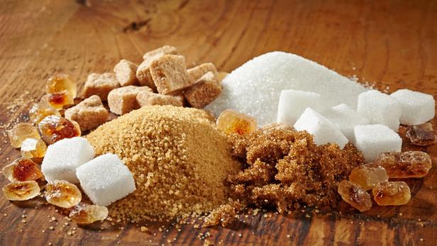 Verschiedene Zuckerarten, darunter weißer, brauner und Kandiszucker, auf einem Holztisch.