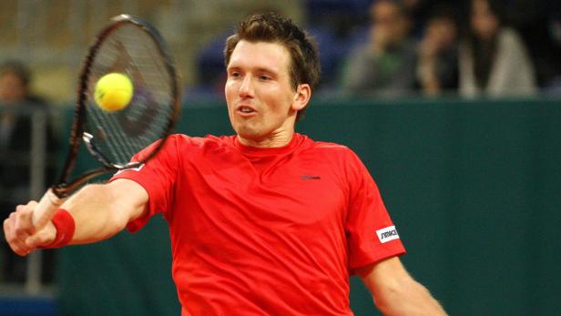 Ein Tennisspieler in rotem Hemd schlägt einen gelben Tennisball.